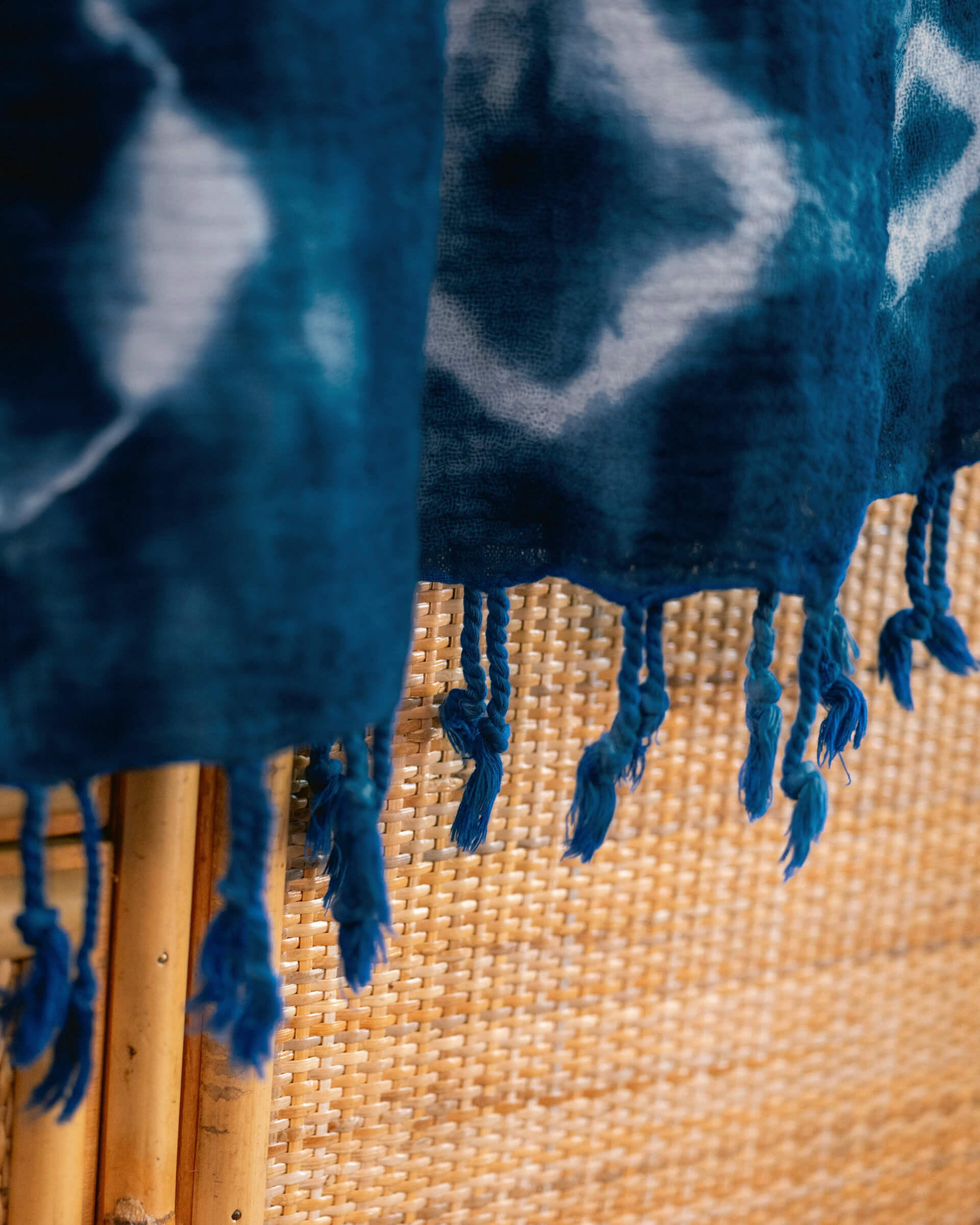 dark blue hand-dyed shibori blanket with fringe draped across a straw panel