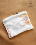 white cactus silk clutch with design laying on brown wooden floor made in morocco 
