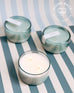 three 7 oz light blue Sea Change canister candles on a blue and white striped background
