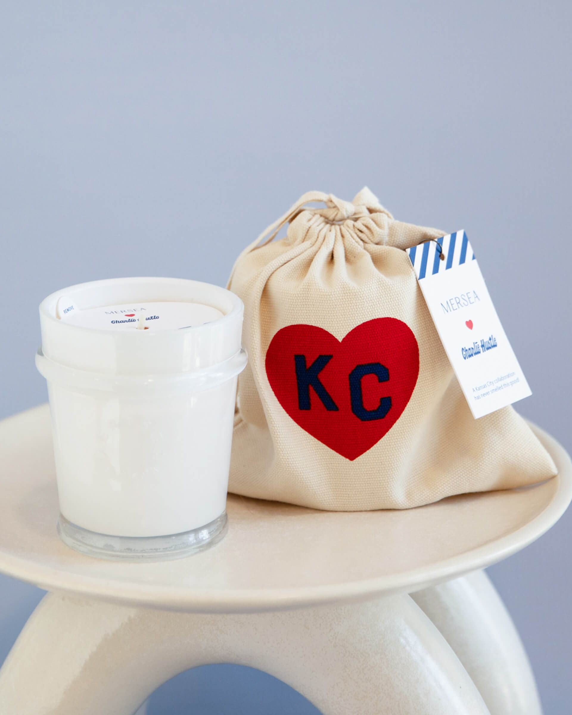 mersea colab coconut sugar candle sitting next to KC inside heart on candle bag on stool