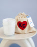 mersea colab coconut sugar candle sitting next to KC inside heart on candle bag on stool