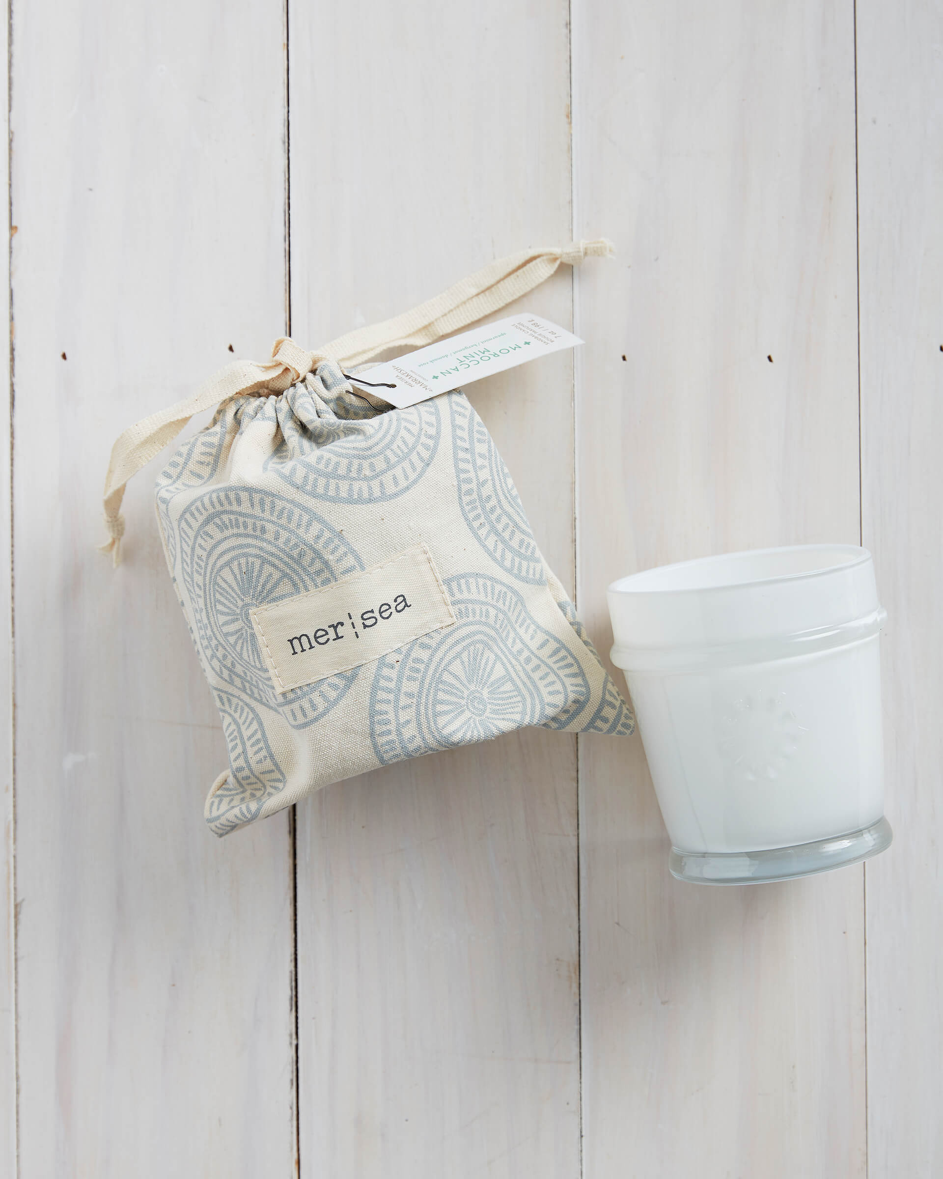 6.5 oz Moroccan Mint sandbag candle in white bag with blue design on a white wood background