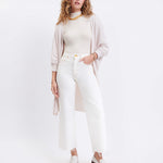 female wearing off white kimono sweater with one hand in her pocket on a white background