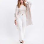 female wearing off white kimono sweater with one hand in her on her head on a white background