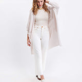 female wearing off white kimono sweater with one hand in her on her head on a white background