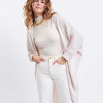 female wearing off white kimono sweater with both hands in her pocket on a white background