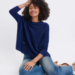 curly haired female wearing dark blue sweater sitting with a hand to her head on a white background