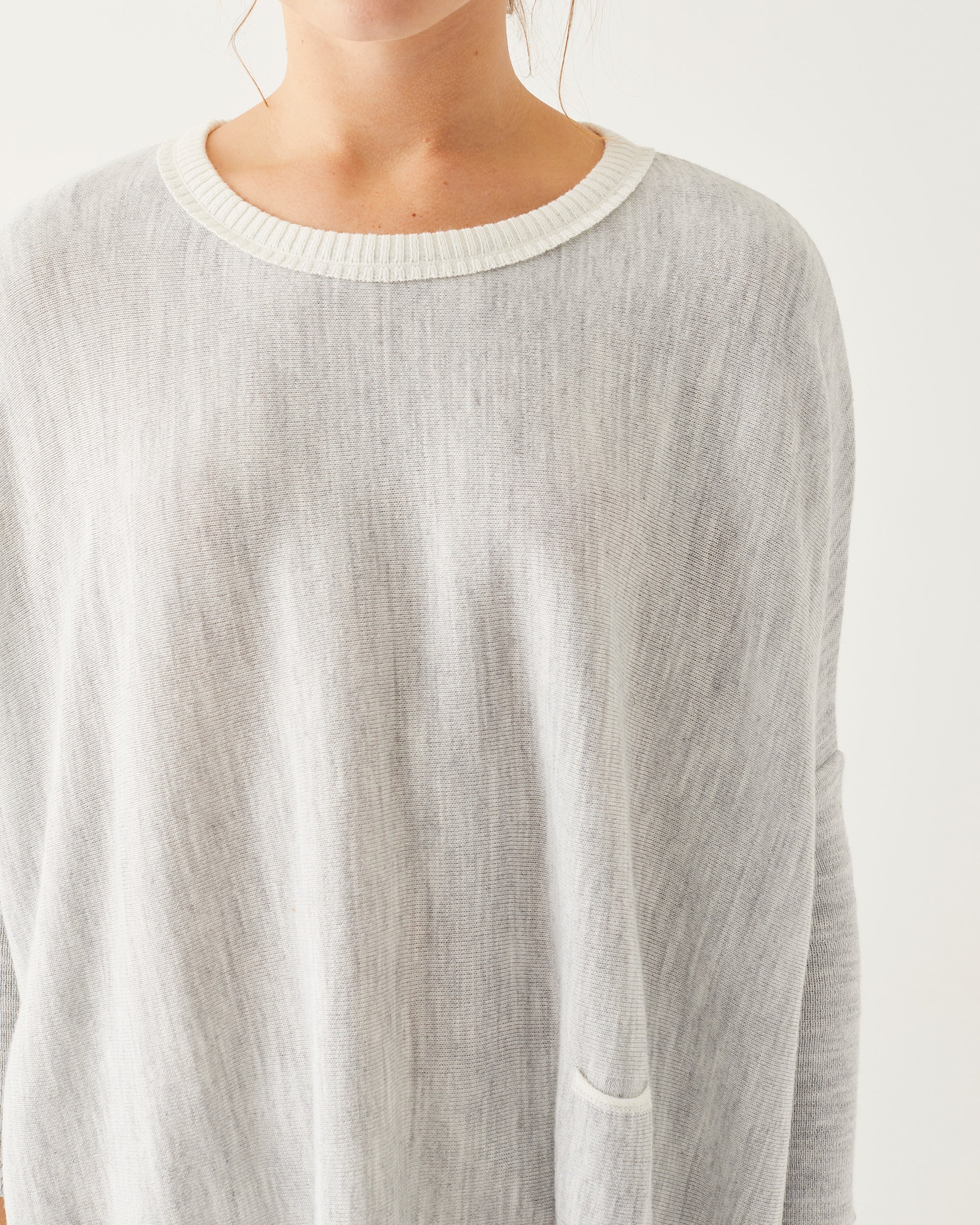 close up of female wearing grey and white sweater focused on crew neckline on a white background
