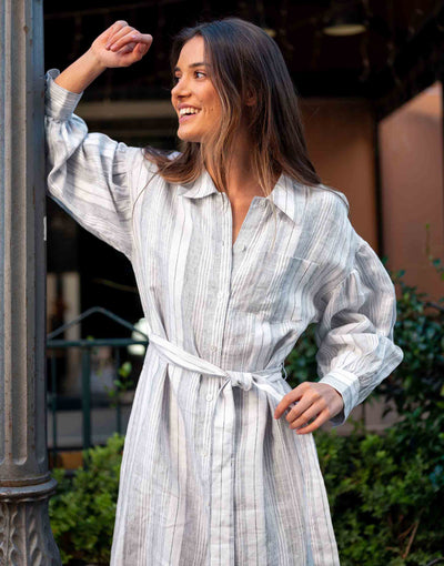 female wearing linen striped collared dress with belt and front buttons leaning against a pole 