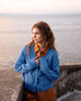 female wearing denim blue buttoned cardigan leaning against a railing looking out at the ocean