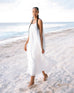 female wearing white maxi dress holding the dress with both hands and walking on the beach 