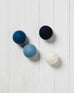 dark blue, light blue and white wool dryer balls laying on a white wood background
