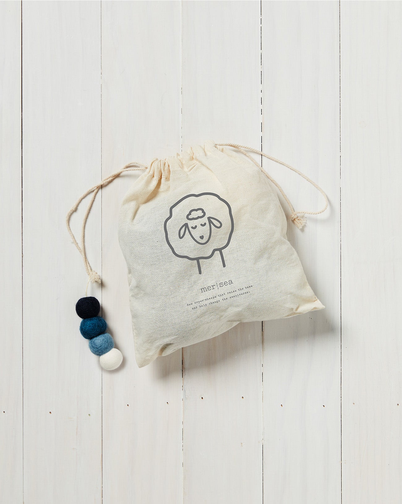 white draw string bag with dark blue, light blue and white wool dryer balls on a white background 