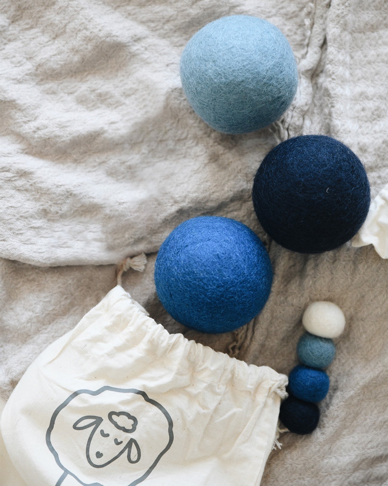 collection of dark blue, light blue and white wool dryer balls laying on a blanket near a bag 