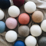 collection of several different colored wool dyer balls laying on top of a neutral blanket 
