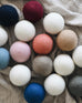 collection of several different colored wool dyer balls laying on top of a neutral blanket 