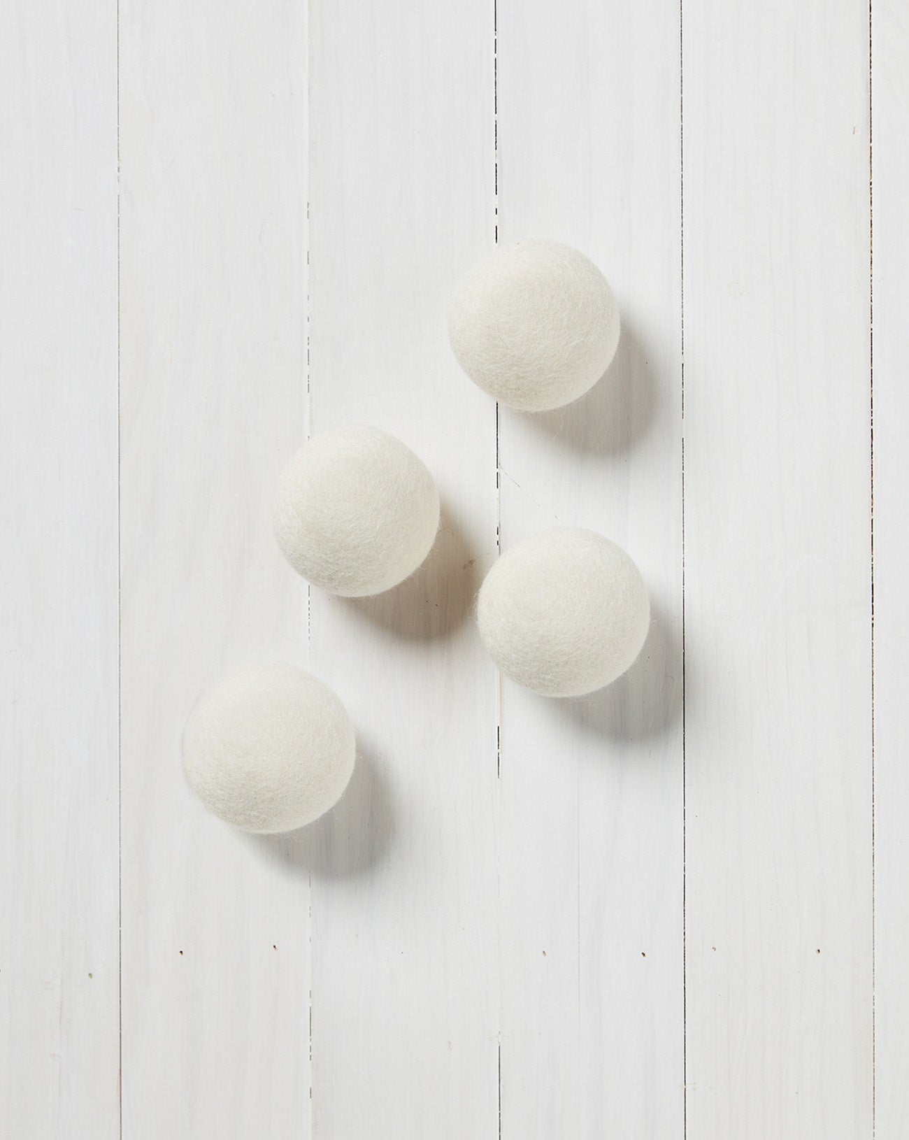 several white wool dryer balls laying on a white wood background