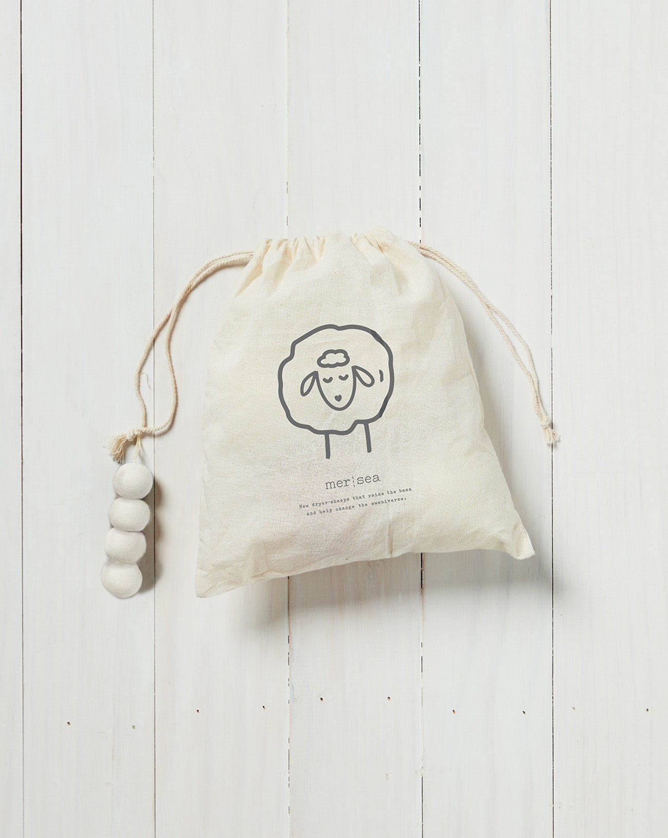 white draw string bag with white wool dryer balls inside on a white background 