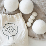 three white wool dryer balls near draw string bag laying on blanket