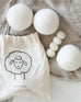 three white wool dryer balls near draw string bag laying on blanket