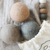 brown, grey, and dark grey wool dryer balls coming out of draw string bag laying on blanket