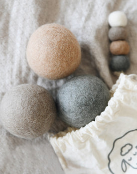 brown, grey, and dark grey wool dryer balls coming out of draw string bag laying on blanket