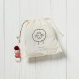 white draw string bag with red, white and pink wool dryer balls inside on a white background 