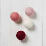 red, white, pink, and light pink wool dryer balls laying on a white wood background