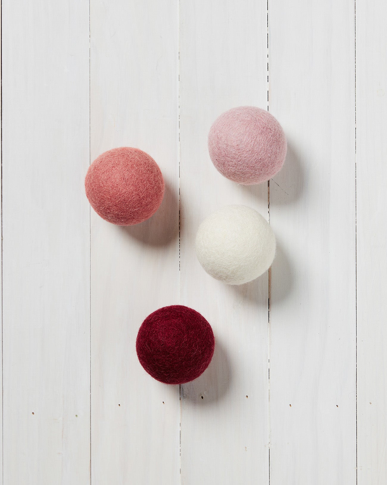 red, white, pink, and light pink wool dryer balls laying on a white wood background