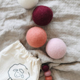 collection of pink, white and red wool dryer balls laying on a blanket near the bag they come in
