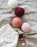 collection of pink, white and red wool dryer balls laying on a blanket near the bag they come in