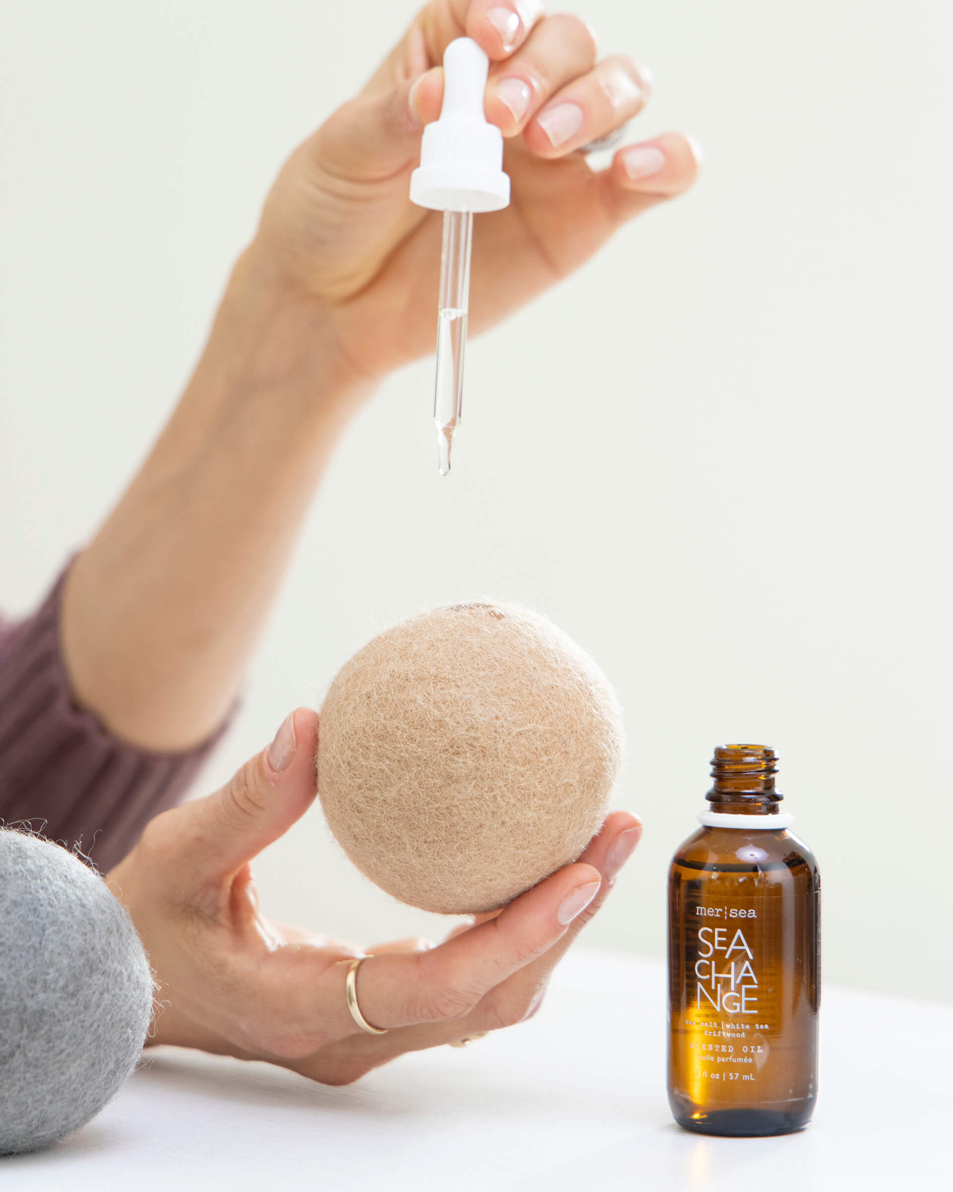 female dropping sea change scented oil onto a neutral wool dryer ball on a white background 