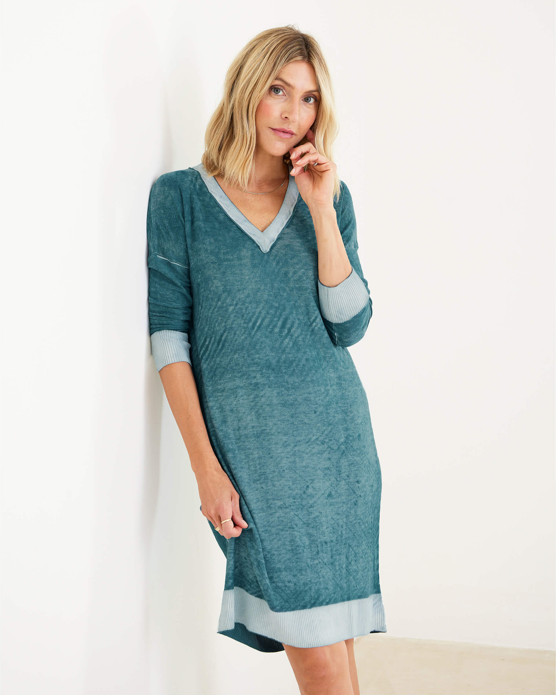 female wearing blue green v-neck long sleeve hand-dyed midi dress leaning on a white wall