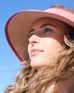 female wearing red straw wide brim hat with opening on top and red trim at the beach