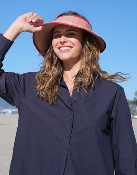 female wearing red straw wide brim hat with opening on top and red trim smiling at the beach