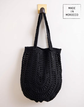 Souk Crochet Tote - Blackblack crochet tote with a long strap and several holes hanging on a hook on a white background