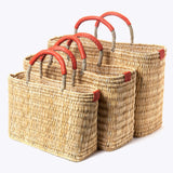 small, medium, large straw basket wrapped with orange leather handles on white background