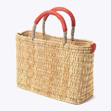 small straw basket wrapped with orange leather handle on a white background at an angle