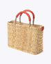 small straw basket wrapped with orange leather handle on a white background at an angle
