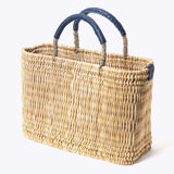 small straw basket wrapped with dark blue leather handle on a white background at an angle