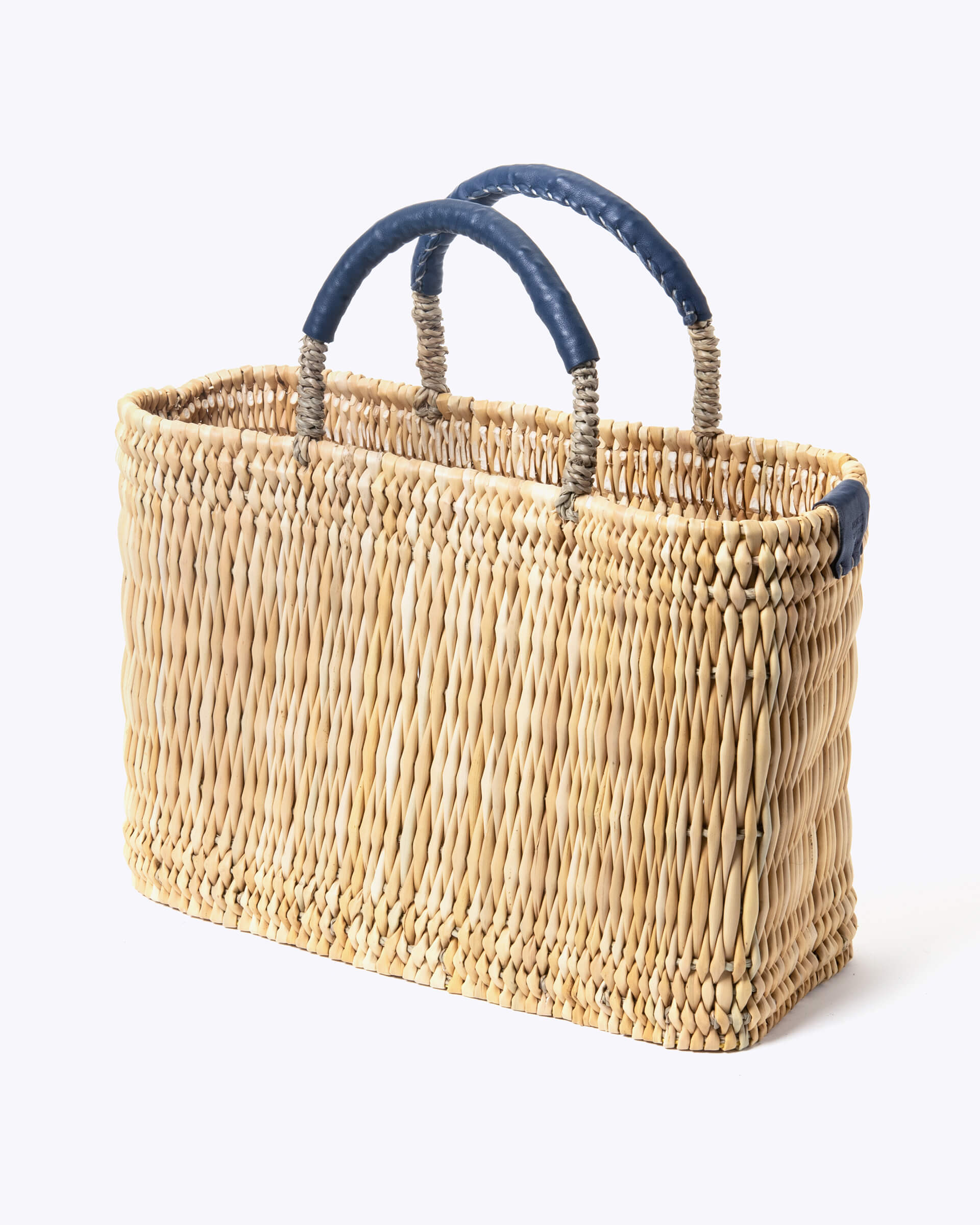 small straw basket wrapped with dark blue leather handle on a white background at an angle