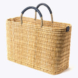 large straw basket wrapped with dark blue leather handle on a white background at an angle