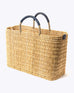 large straw basket wrapped with dark blue leather handle on a white background at an angle