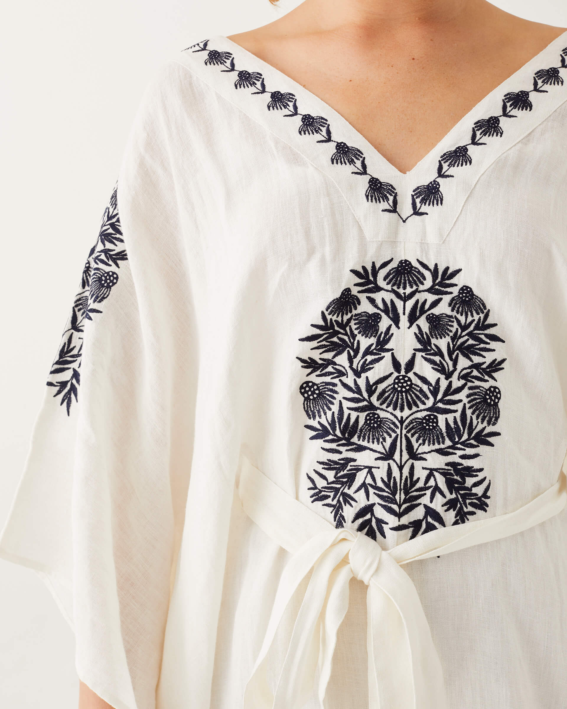 front detail of female wearing white and blue embroidered kaftan with v-neck on a white background