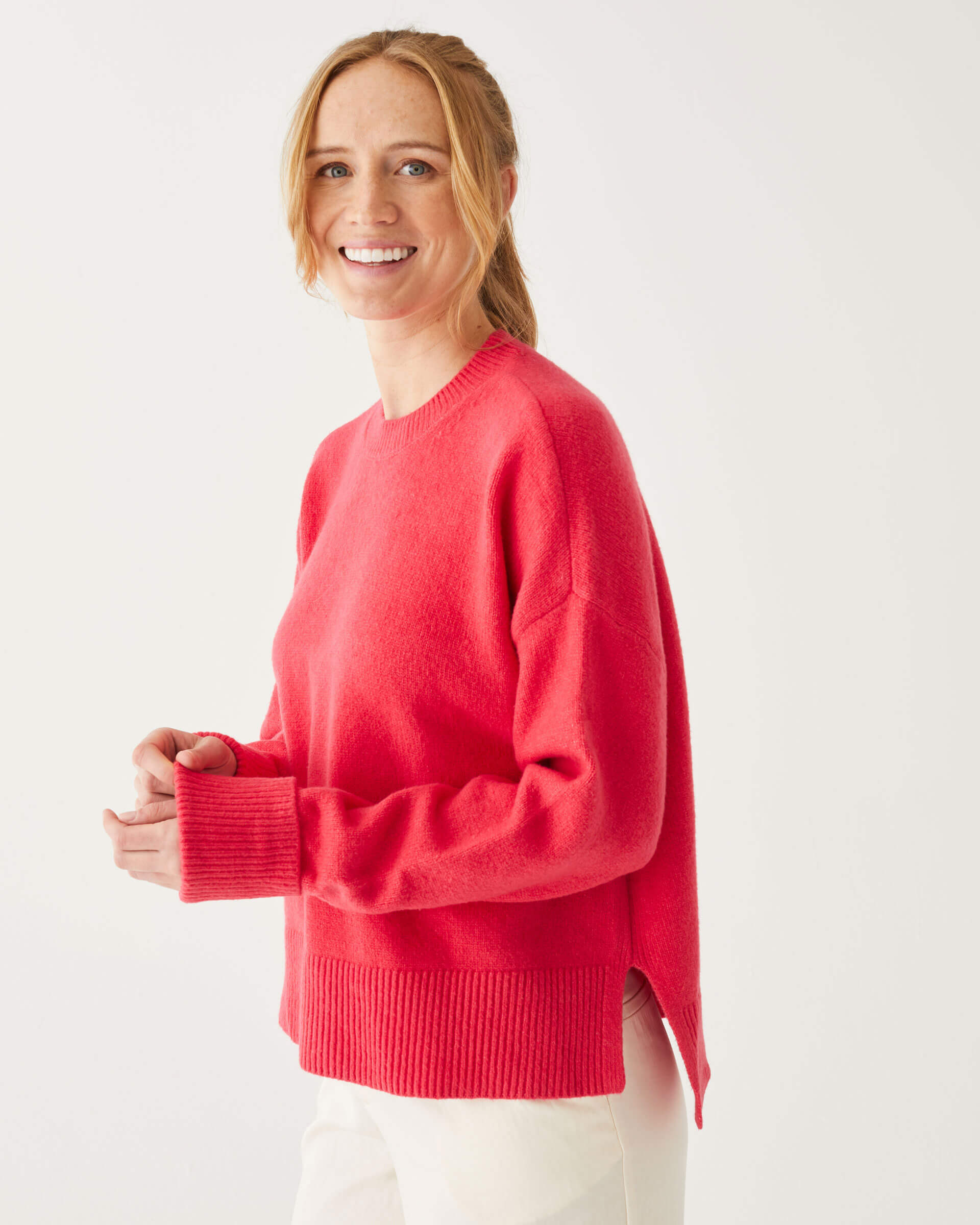 female wearing red crewneck sweater standing slightly to the side in front of a white background
