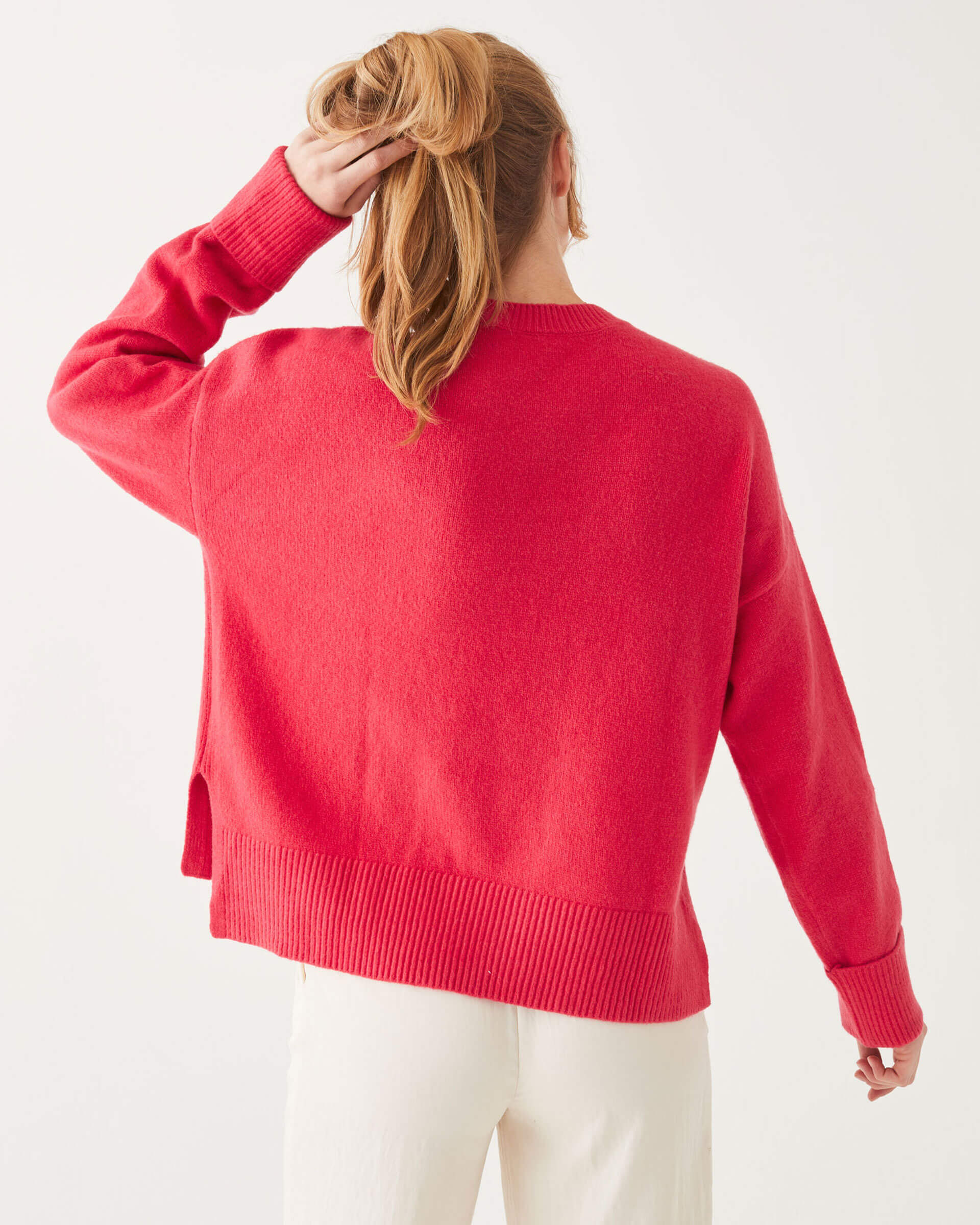 female wearing red crewneck sweater standing backwards holding her hair on a white background