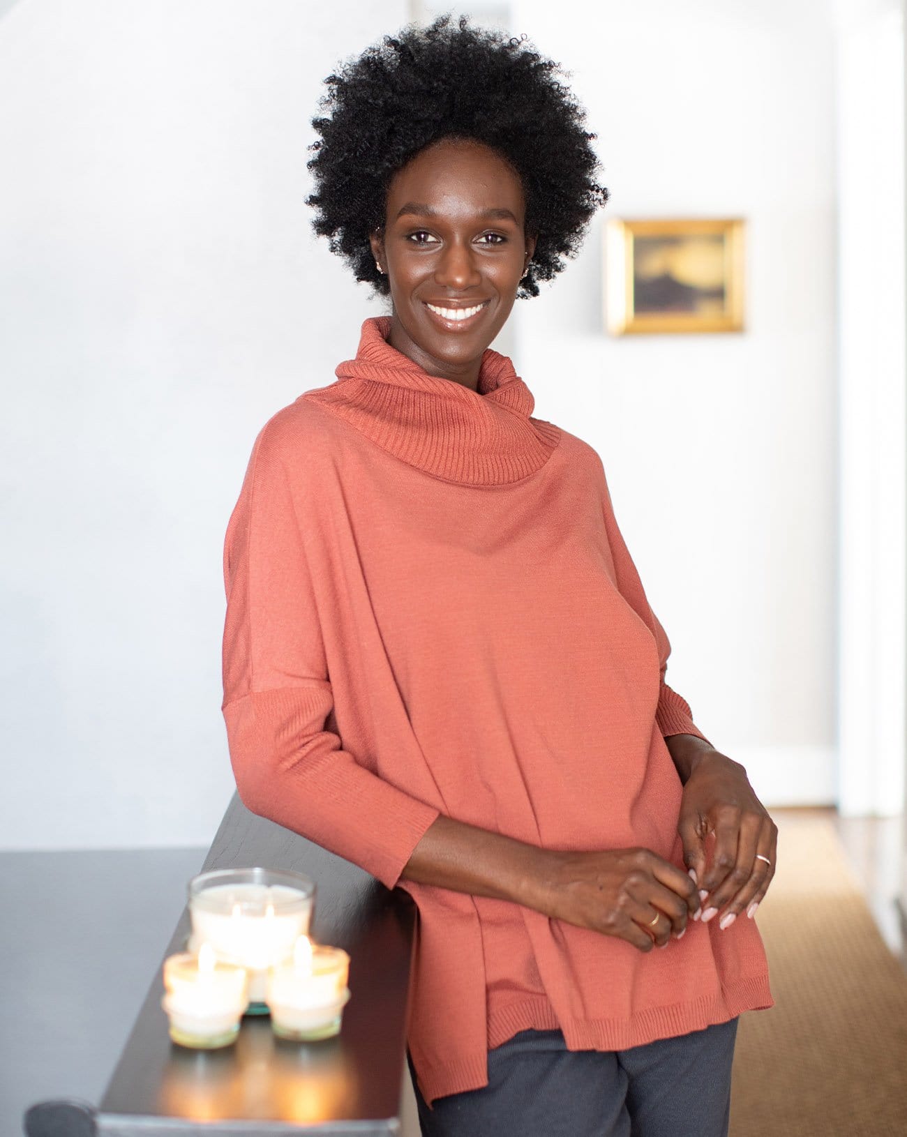 woman relaxing  wearing mersea newport sweater in sienna color with a split front turtleneck and ribbed sleeves.
