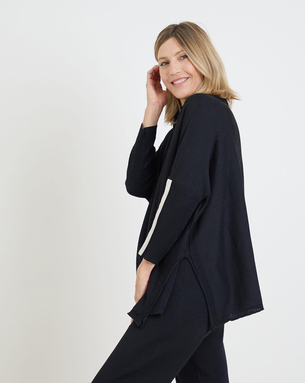side view of woman wearing mersea newport sweater in black with white accent stripe down lower sleeve with a split front turtleneck and ribbed sleeves