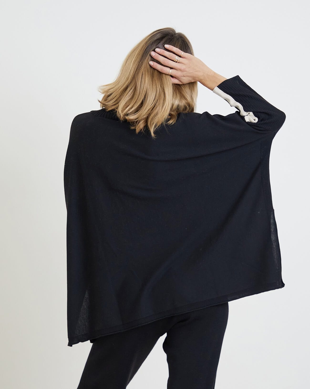 rearview of woman wearing mersea newport sweater in black with white accent stripe down lower sleeve with a split front turtleneck and ribbed sleeves