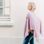 female wearing light pink wrap over her shoulders walking outside in front of a white building
